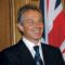 Tony Blair smiling in front of a United Kingdom flag.